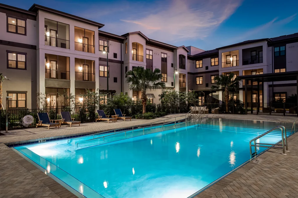inground pool outside senior living community at night with palm trees