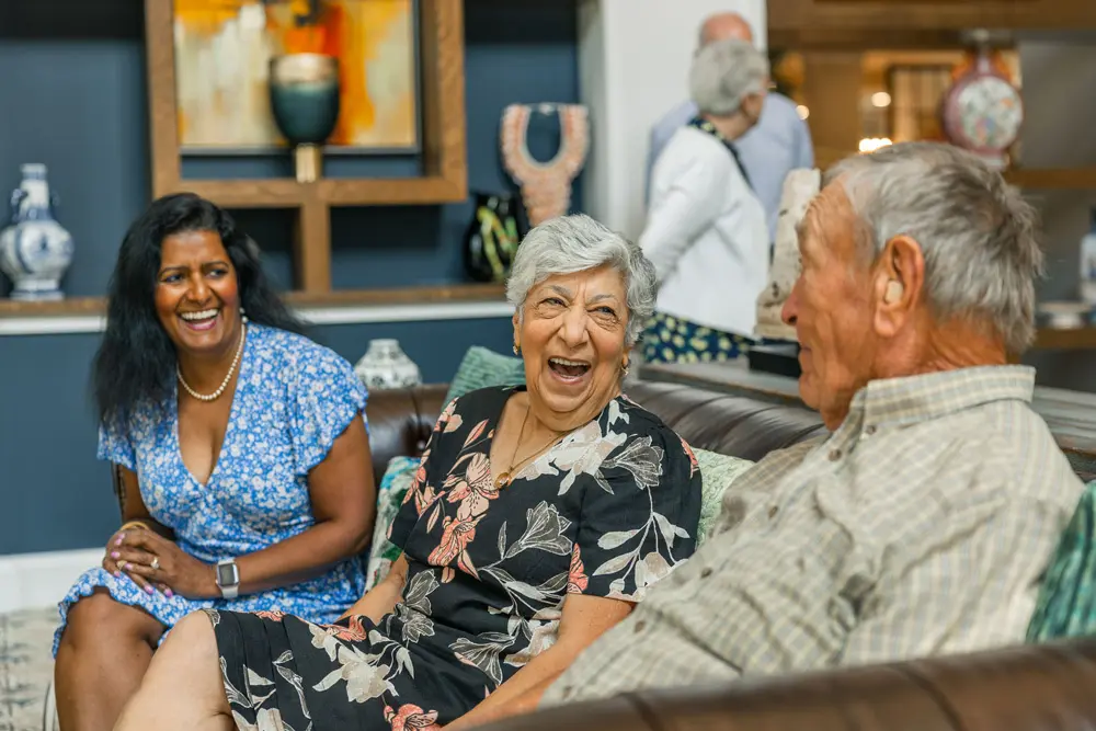 Three seniors laughing and talking on a couch in a senior living community in Mechanicsville, Virginia